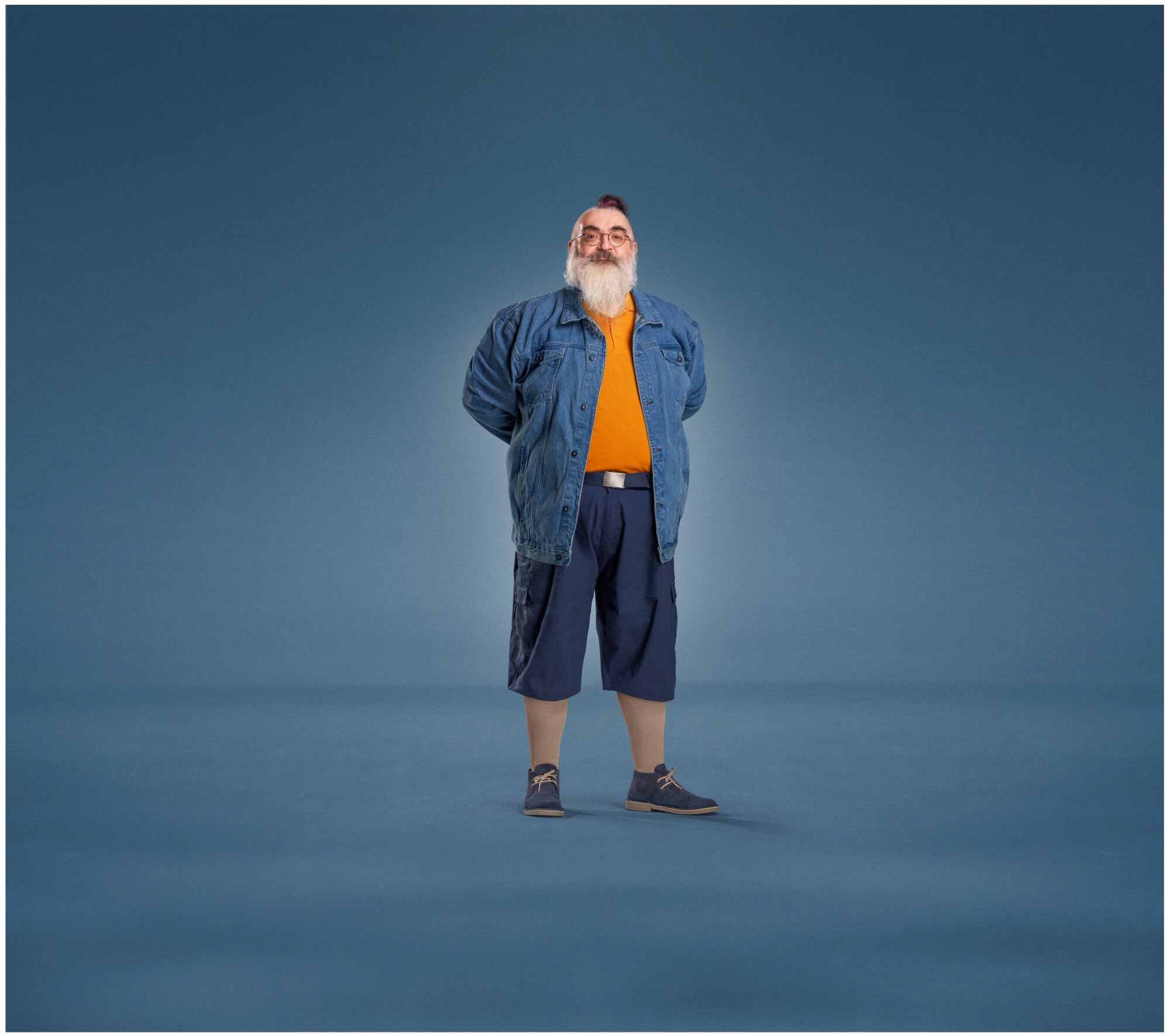 A bearded man wearing a denim jacket, orange shirt, navy shorts, and sneakers, paired with JOBST UlcerCare compression socks.